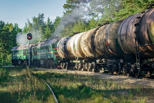 Freight train with tank wagons in forest. Green cargo locomotive