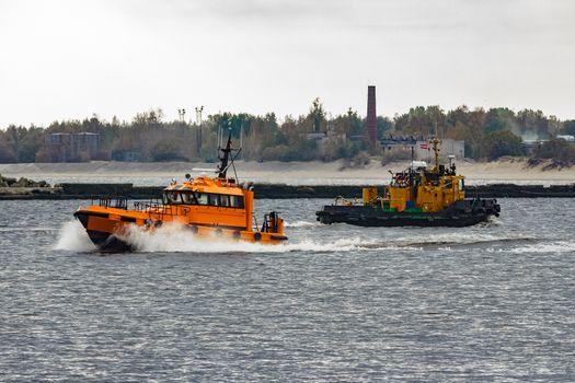 Orange pilot ship moving at speed past the tug ship in Riga