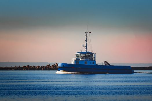 Blue small tug ship sailing past the breakwater dam in morning