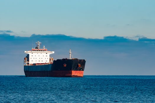 Black cargo ship moving in still Baltic sea water. Riga, Europe