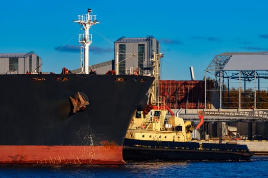 Black cargo ship mooring at the port with tug ship support