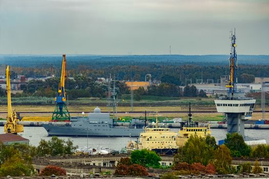 Military ship sailing past the cargo port in Riga, Latvia