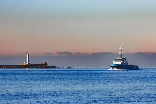 Blue small tug ship sailing past the breakwater dam in morning