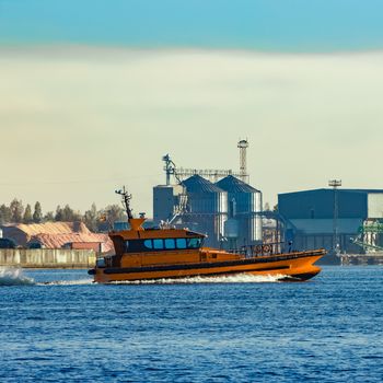 Orange pilot ship sailing past the factory in Latvia