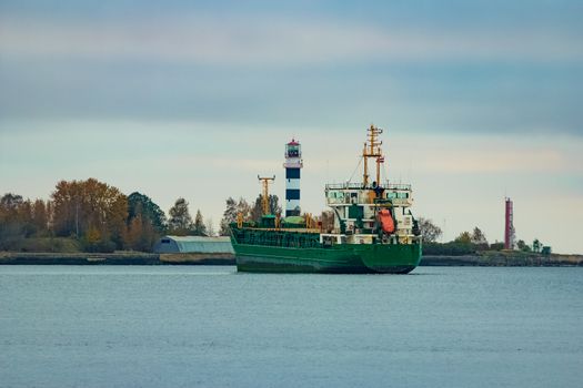 Green cargo ship moving to the port in cloudy day