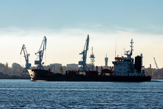 Black cargo oil tanker moving past the cargo cranes