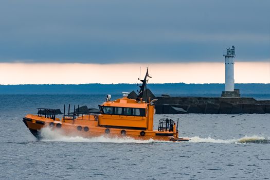 Orange pilot ship moving at speed past the lighthouse in Riga