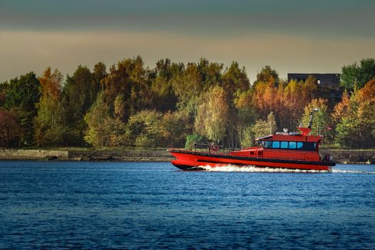 Red pilot ship moving past the autumn trees in Europe