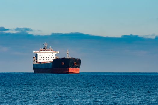 Black cargo ship moving in still Baltic sea water. Riga, Europe