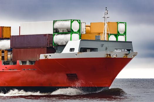 Red cargo container ship's bow in cloudy day