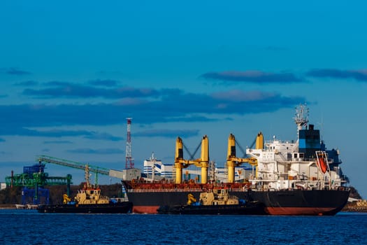 Black cargo ship mooring at the port with tug ship support