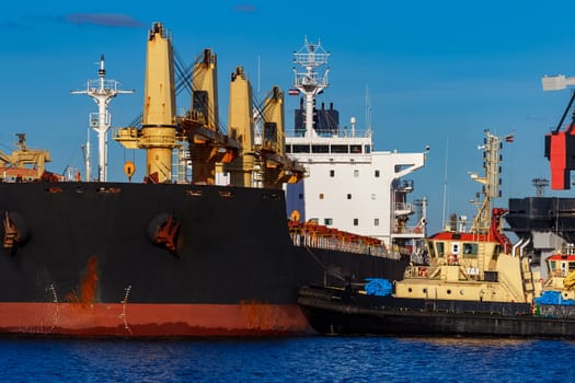 Black cargo ship mooring at the port with tug ship support