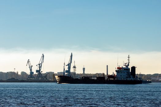 Black cargo oil tanker moving past the cargo cranes