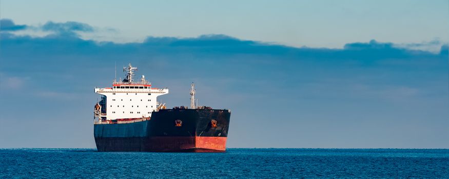 Black cargo ship moving in still Baltic sea water. Riga, Europe