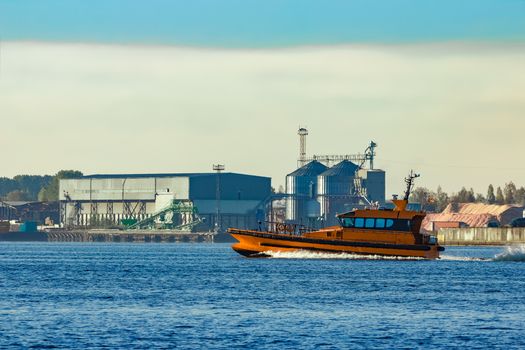 Orange pilot ship sailing past the factory in Latvia