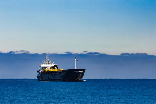 Black cargo ship with long reach excavator moving by baltic sea