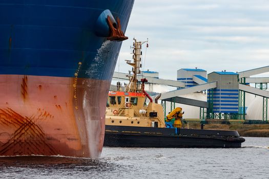 Tug ship towing blue bulk carrier in the port of Riga