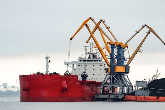 Large red cargo ship loading with a coal in the port