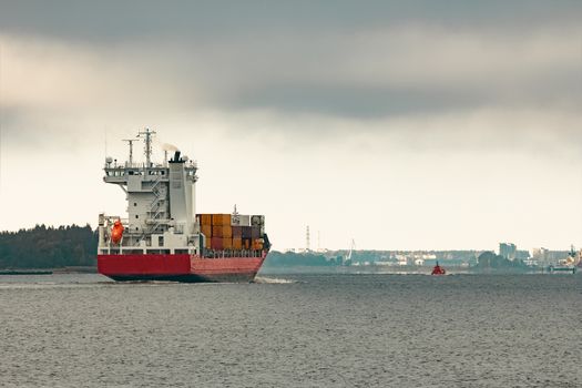 Red cargo container ship entering the port of Riga in cloudy day