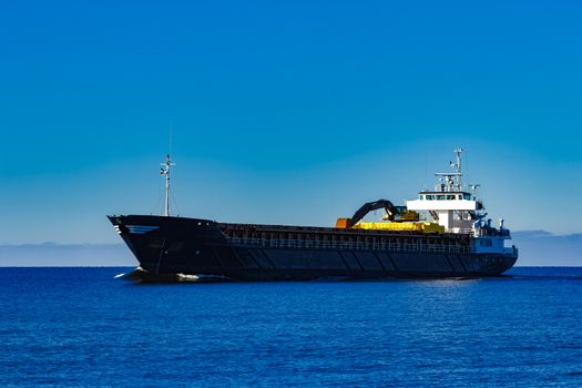 Black cargo ship with long reach excavator moving by baltic sea