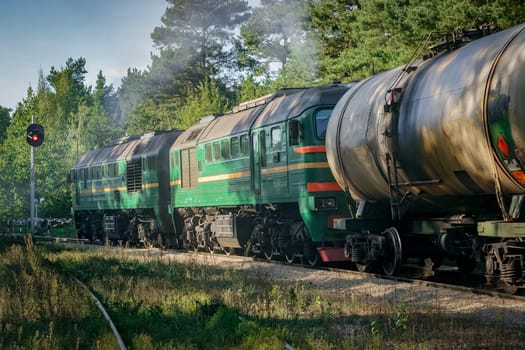 Freight train with tank wagons in forest. Green cargo locomotive