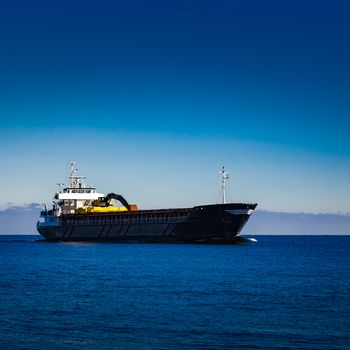 Black cargo ship with long reach excavator moving by baltic sea