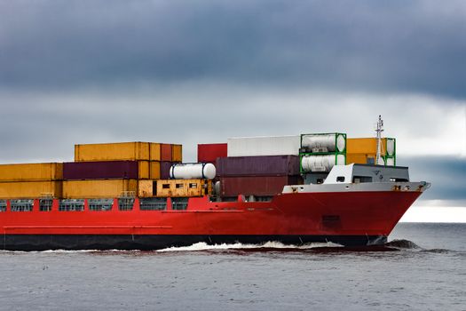 Red cargo container ship's bow in cloudy day