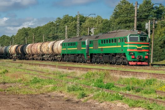 Freight train with tank wagons in forest. Green cargo locomotive