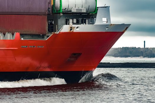 Red cargo container ship's bow in cloudy day