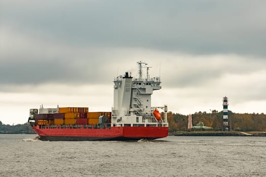 Red cargo container ship entering the port of Riga in cloudy day