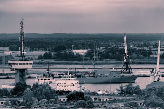 Military ship sailing past the cargo port in Riga, Latvia