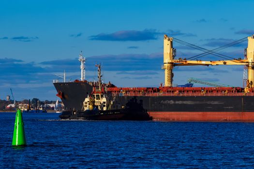 Black cargo ship mooring at the port with tug ship support