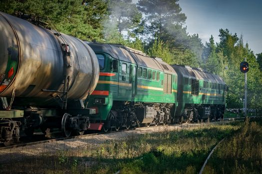 Freight train with tank wagons in forest. Green cargo locomotive