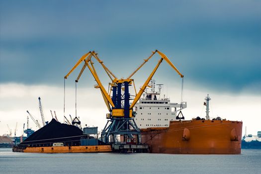 Large orange cargo ship loading with a coal in the port