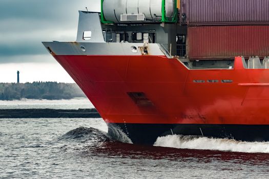 Red cargo container ship's bow in cloudy day