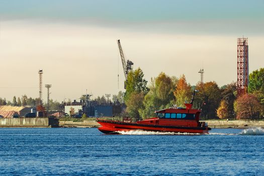 Red pilot ship moving past the autumn trees in Europe