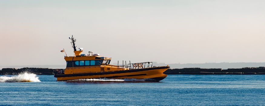 Orange pilot ship moving at speed past the breakwater dam