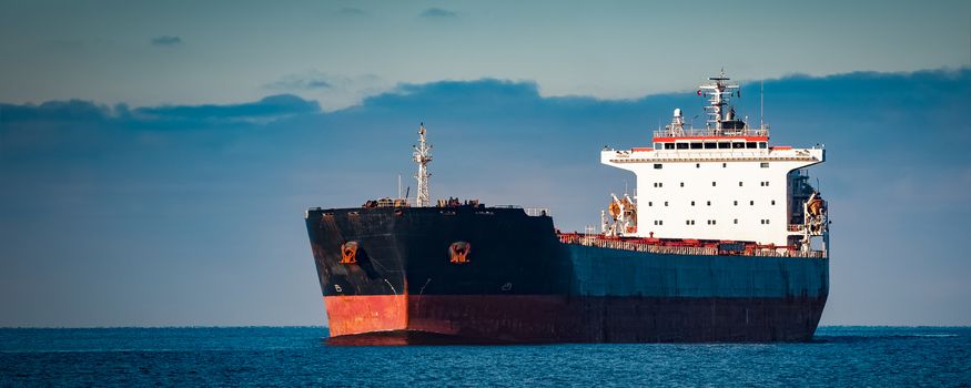 Black cargo ship moving in still Baltic sea water. Riga, Europe