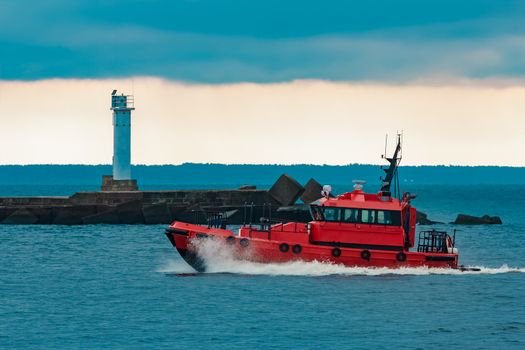 Red pilot ship moving at speed past the lighthouse in Riga