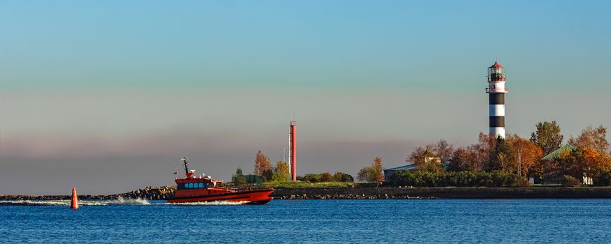 Red pilot ship moving past the lighthouse in Riga