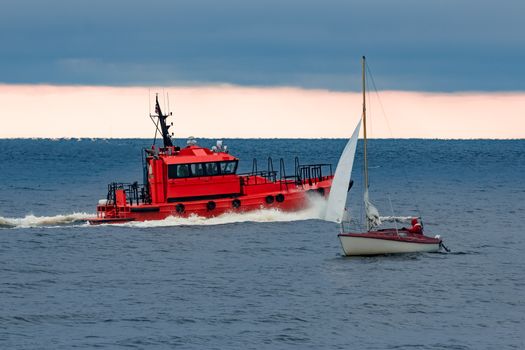 Red pilot ship moving at speed past the sailboat in Baltic sea
