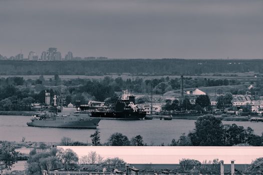 Military ship sailing past the cargo port in Riga, Latvia