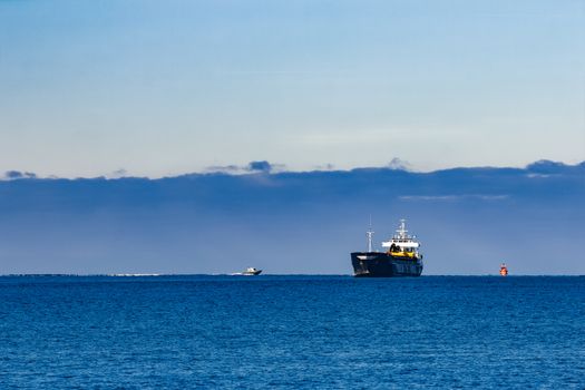 Black cargo ship with long reach excavator moving by baltic sea