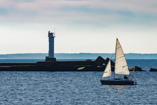 Small sailboat traveling past the lighthouse in sunny day