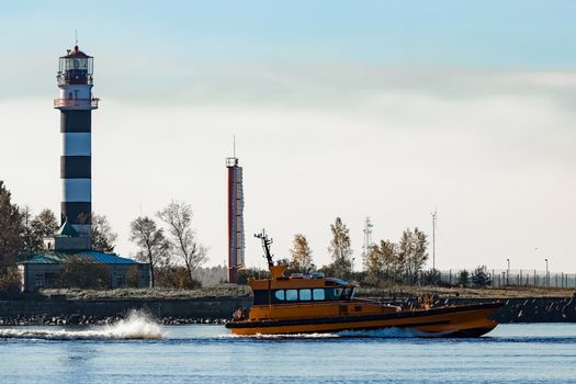 Orange pilot ship sailing past the lighthouse in Riga