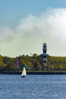 Small sailboat traveling past the lighthouse in sunny day