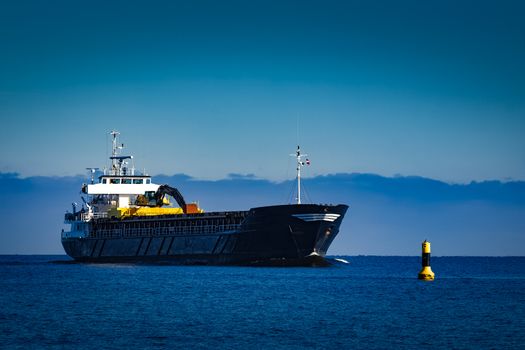 Black cargo ship with long reach excavator moving by baltic sea