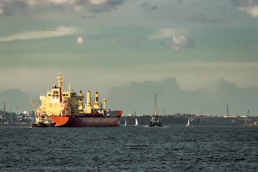 Red cargo ship and the tug ship towing it to the port