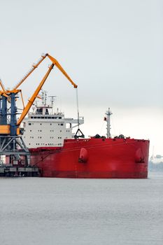 Large red cargo ship loading with a coal in the port