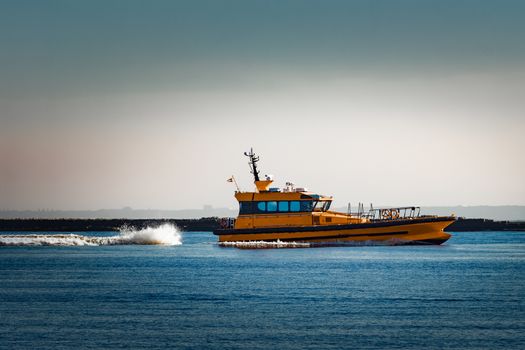 Orange pilot ship moving at speed past the breakwater dam